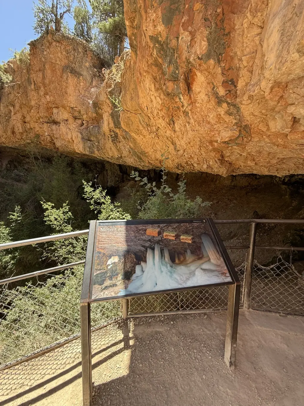Mossy Cave with a trail sign and overhanging orange rock