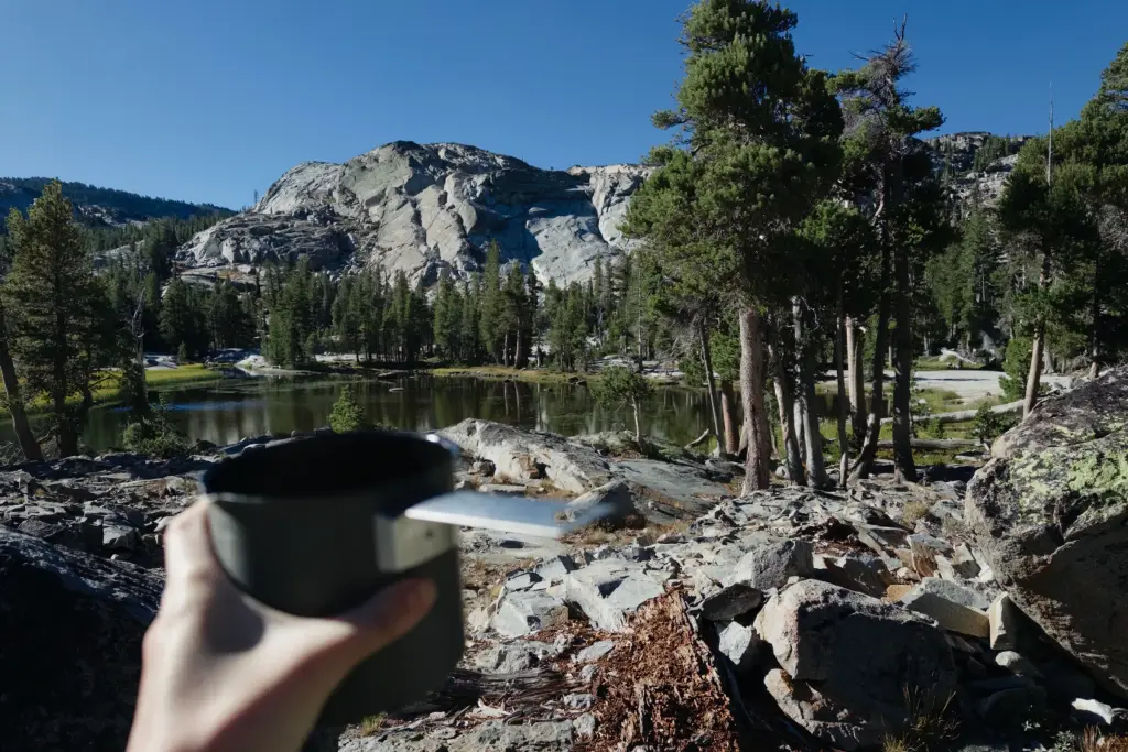 A cup held in front of Upper Velma Lake and the granite above it